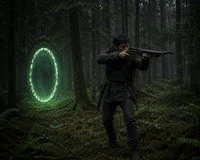 a man holding a gun in the woods with a glowing circle in the background